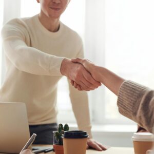 Two people shaking hands over a table during a meeting.